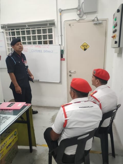 KSD Security trainer leading a customer-entrance briefing in the AEON Falim CCTV control room during the OCW training