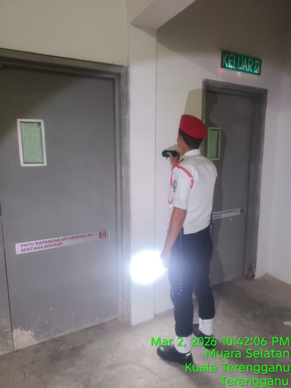 KSD Security guard with red beret checking fire exit doors with a flashlight during a night patrol at Muara Selatan, Kuala Terengganu.