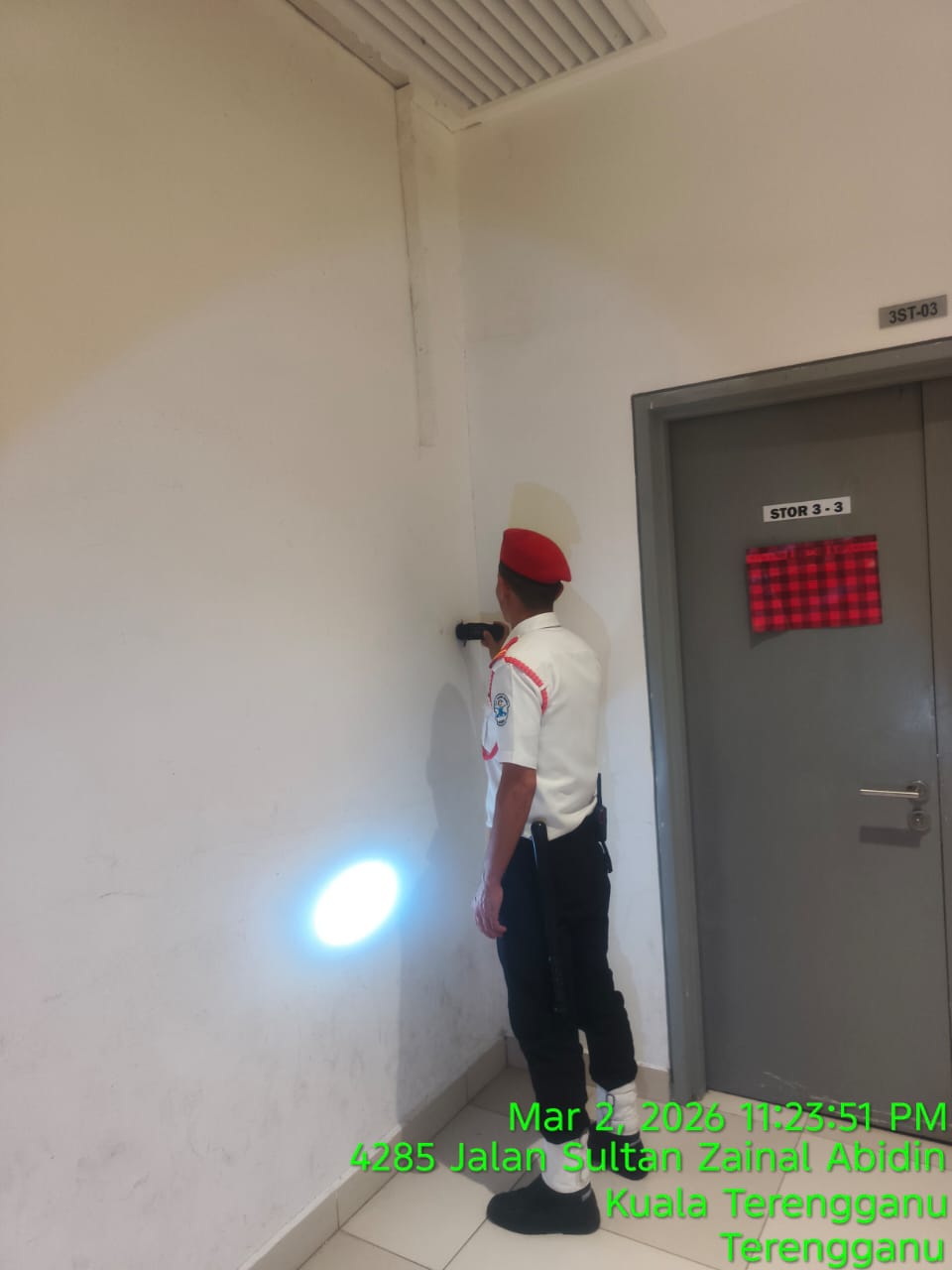 KSD Security guard in red beret inspecting a storeroom door and wall with a flashlight during a night patrol at Jalan Sultan Zainal Abidin, Kuala Terengganu.